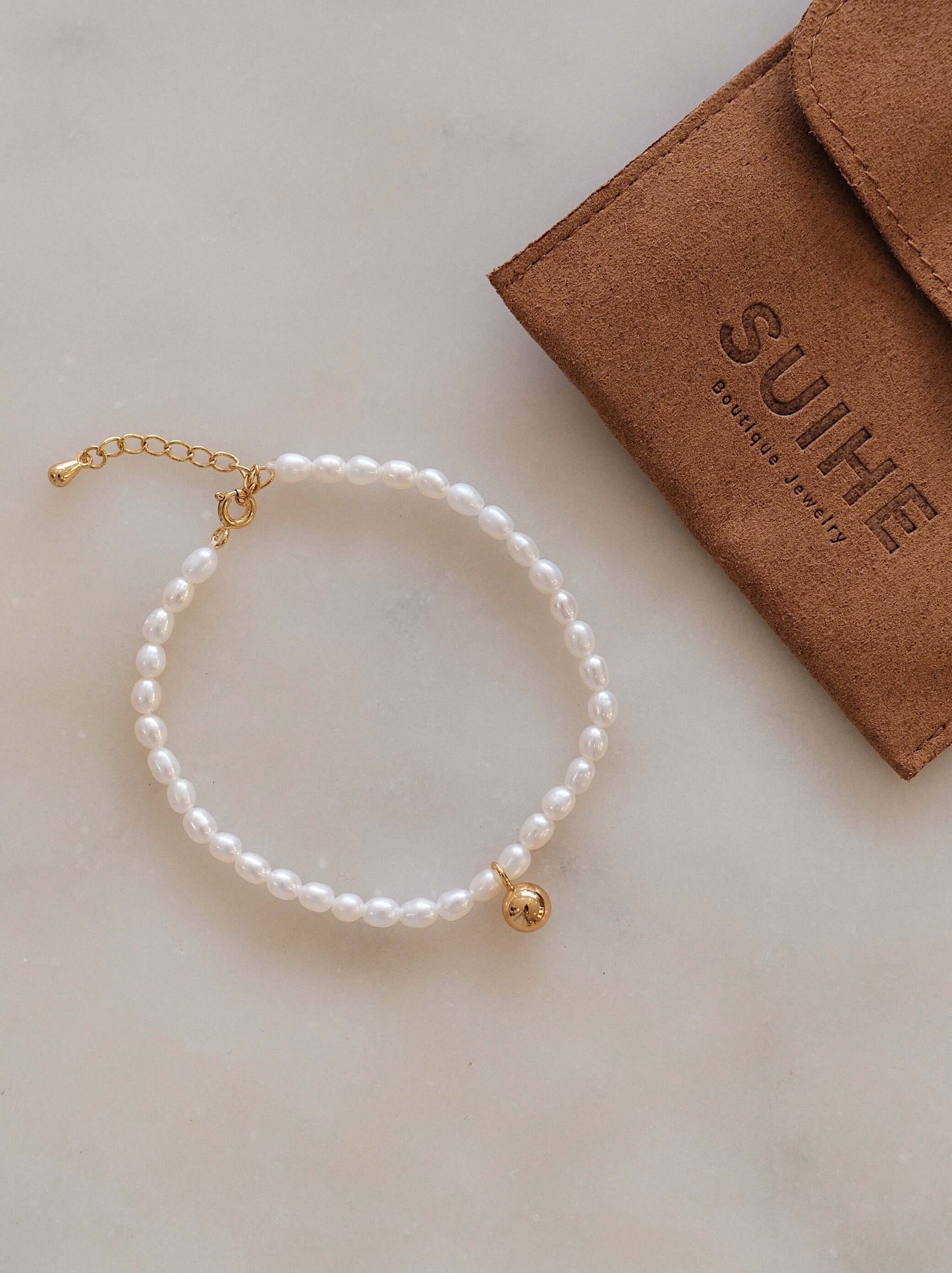 Celestia Freshwater Pearl Bracelet with gold-tone charm by SUIHE Jewelry, displayed on a marble surface with branded pouch.