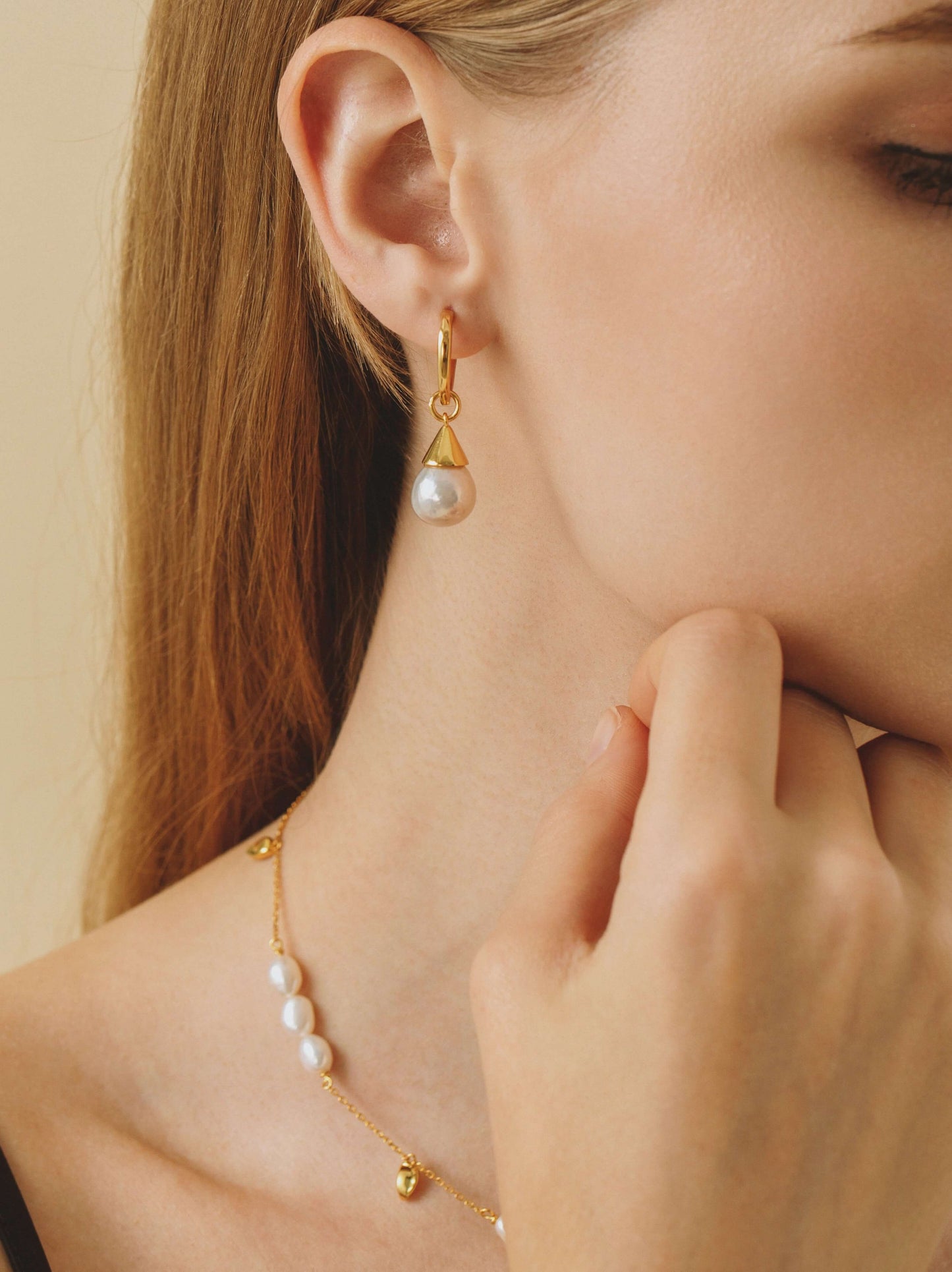 Close-up of a woman's ear wearing "Dewdrop" freshwater pearl earrings by SUIHE Jewelry, featuring gold-plated sterling silver and pearls.