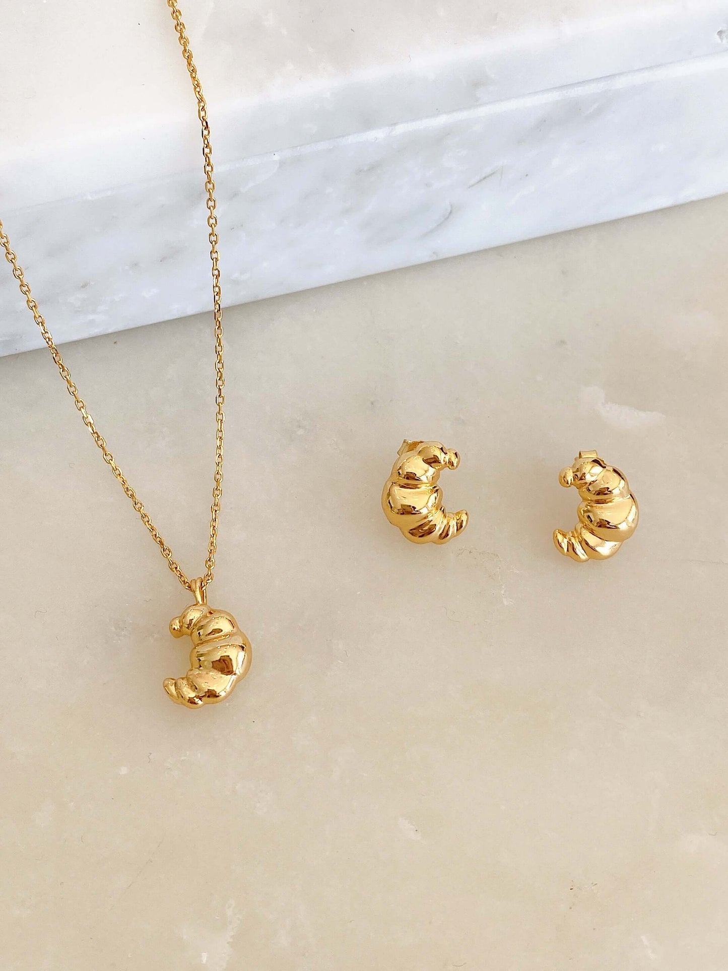 SUIHE Jewelry "Croissant" Necklace in 18k Gold Vermeil, featuring a textured croissant charm, evoking Parisian elegance on marble surface.