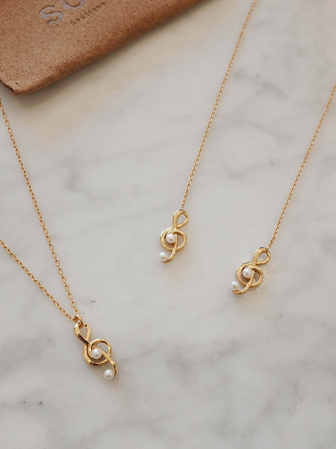 Gold vermeil and pearl jewelry set by SUIHE Jewelry on a marble surface, featuring elegant intertwined designs.