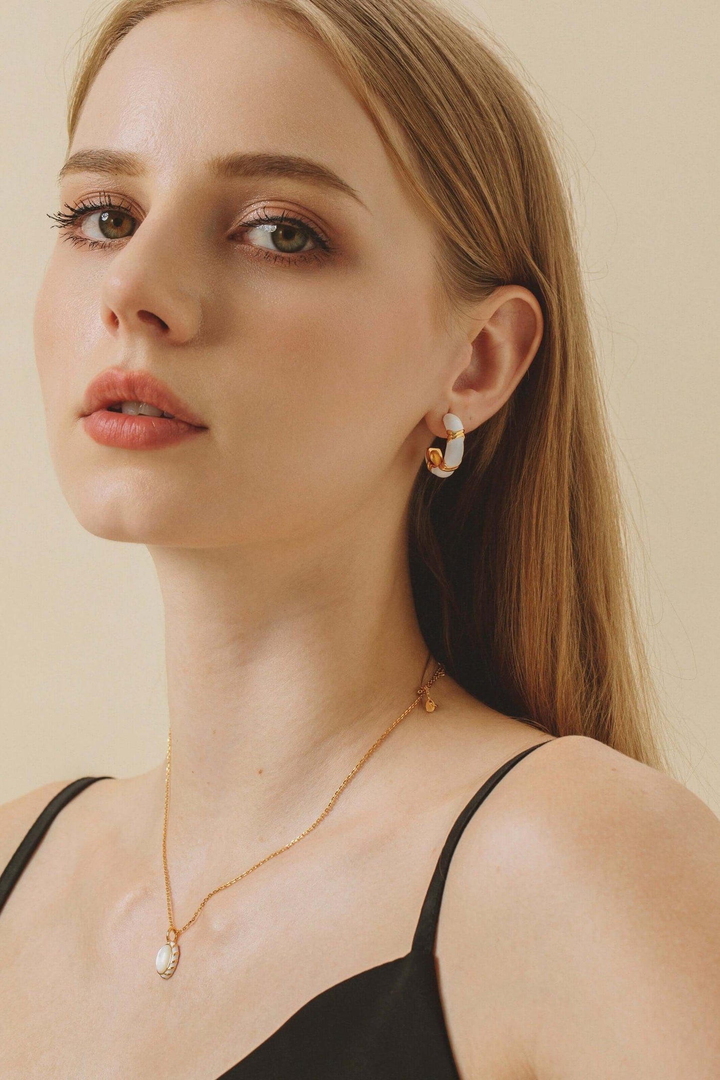 Model wearing Luna white enamel hoop earrings by SUIHE Jewelry with gold vermeil accents, showcasing elegance and sophistication.