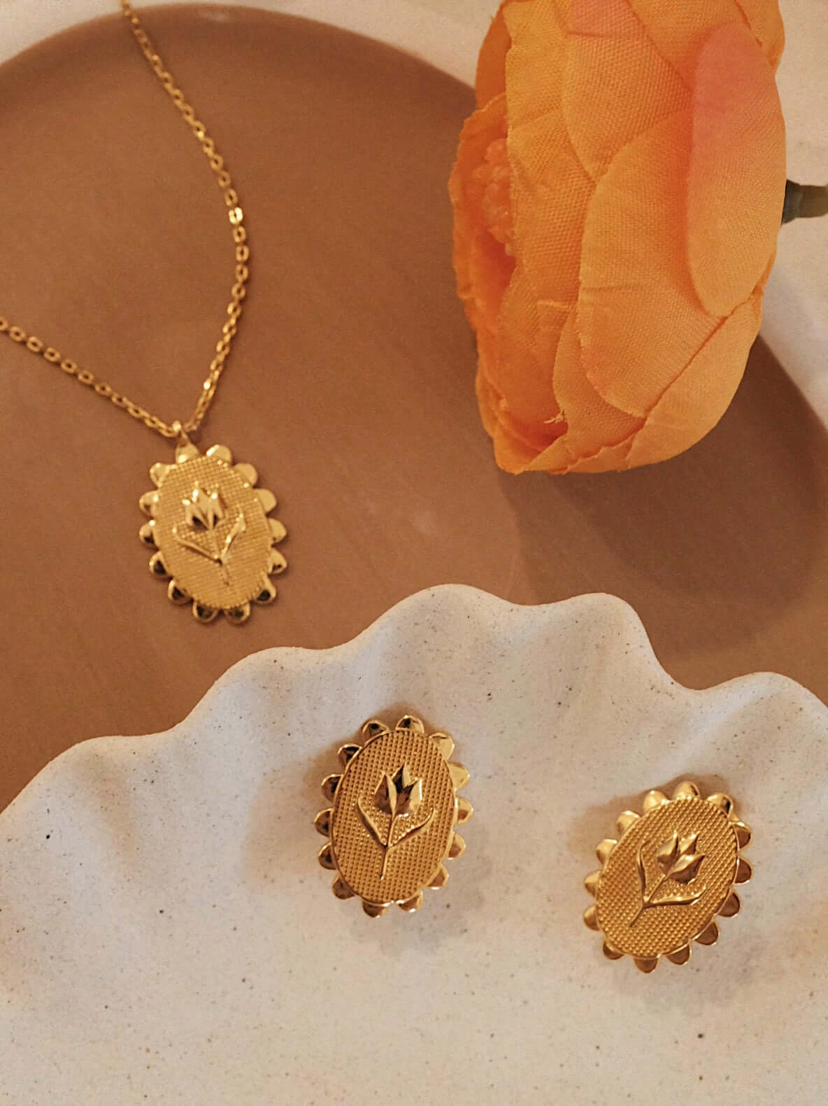 18k Gold Vermeil "Golden Tulip" earrings by SUIHE Jewelry displayed on a textured plate next to a matching necklace and orange flower.