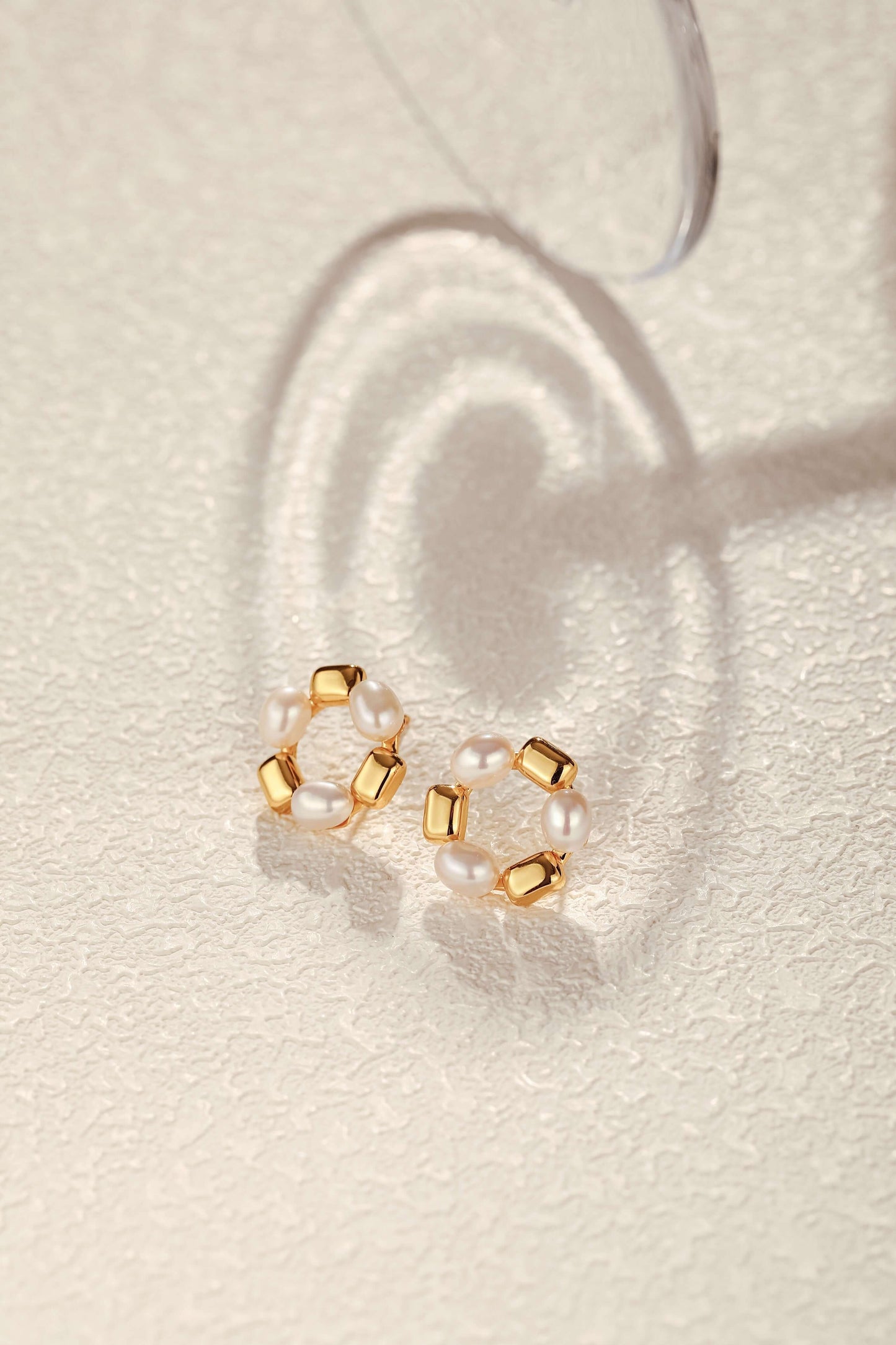 SUIHE Jewelry "Jellybean" freshwater pearl hoop earrings with 18k gold vermeil and copper accents on textured surface.