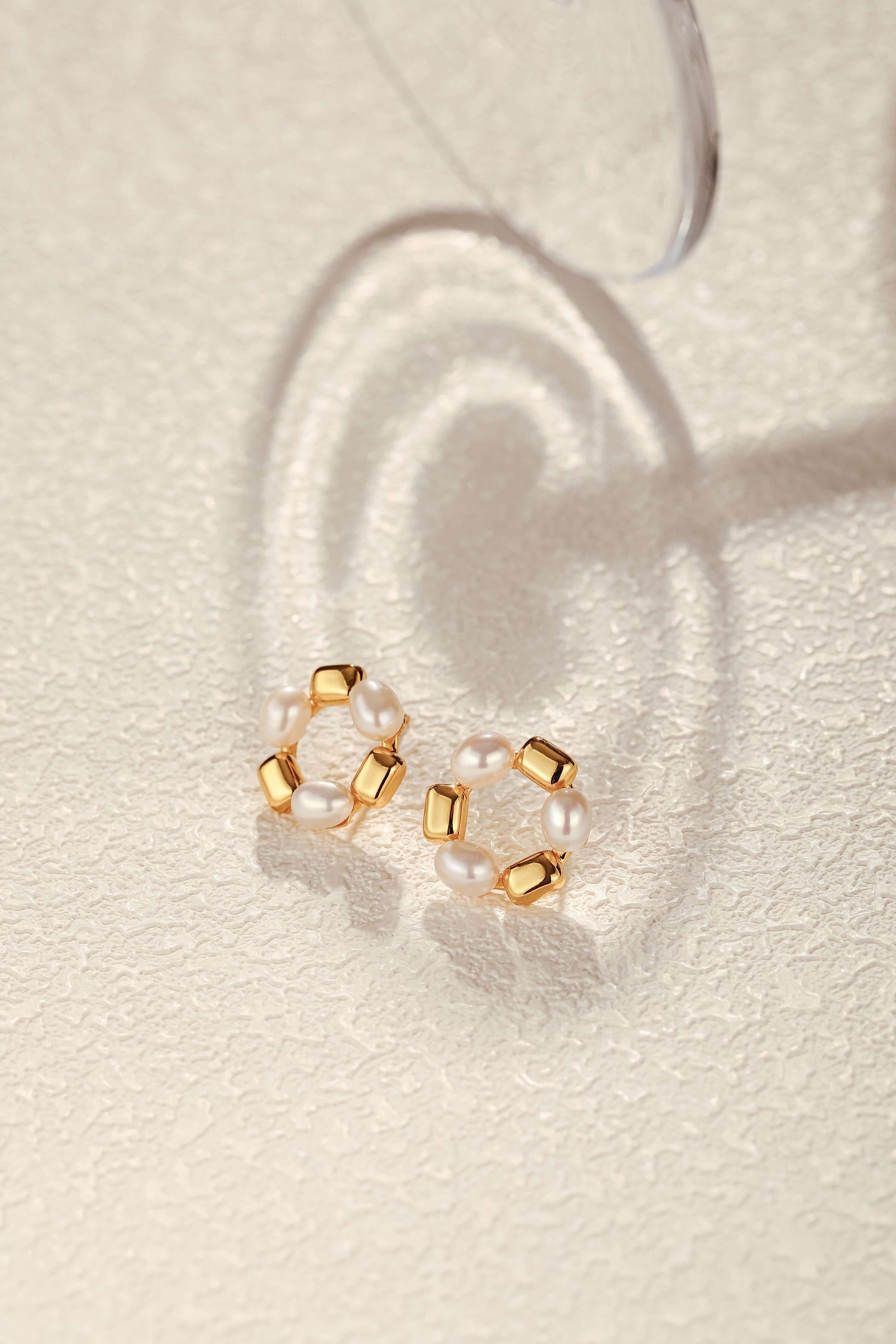 SUIHE Jewelry "Jellybean" freshwater pearl hoop earrings with 18k gold vermeil and copper accents on textured surface.