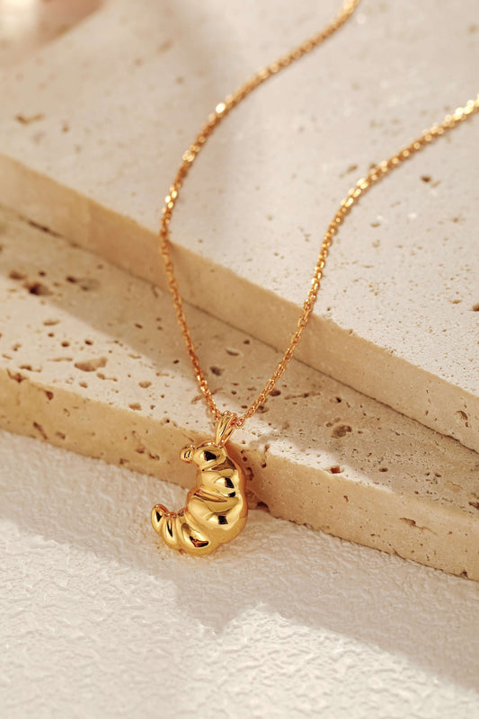 Croissant necklace in 18k gold vermeil, SUIHE Jewelry, showcasing a textured croissant design on rustic stone surface.