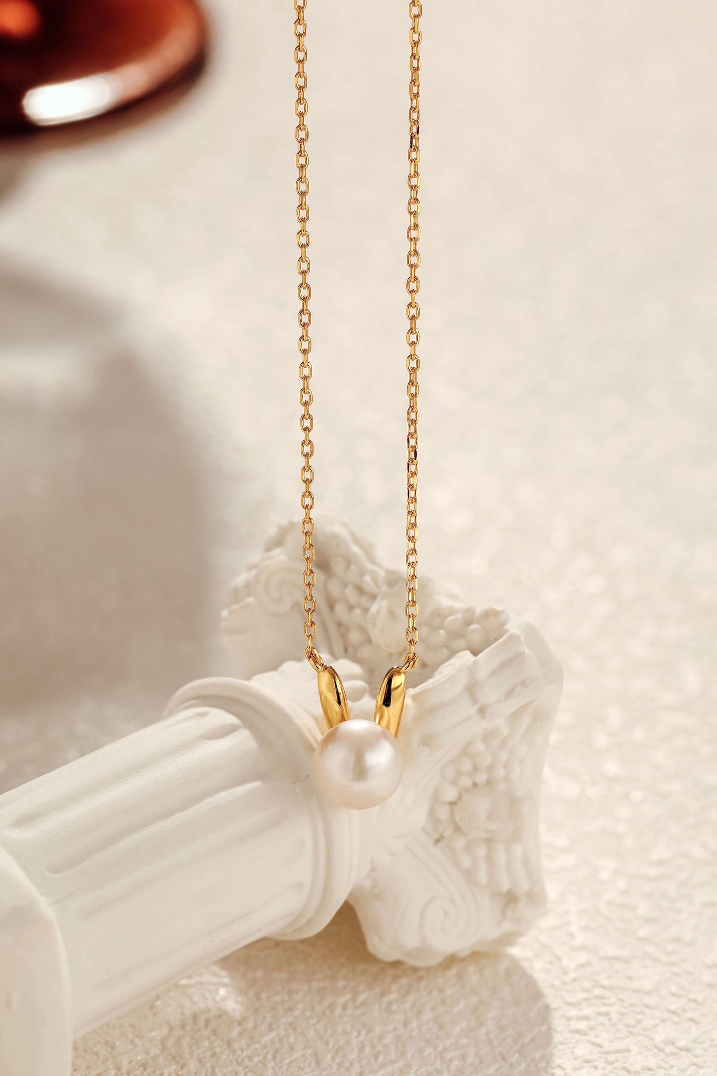 Bunny Freshwater Pearl Necklace on 18k Gold Vermeil chain, SUIHE Jewelry, showcasing elegance and whimsy on a decorative pillar.