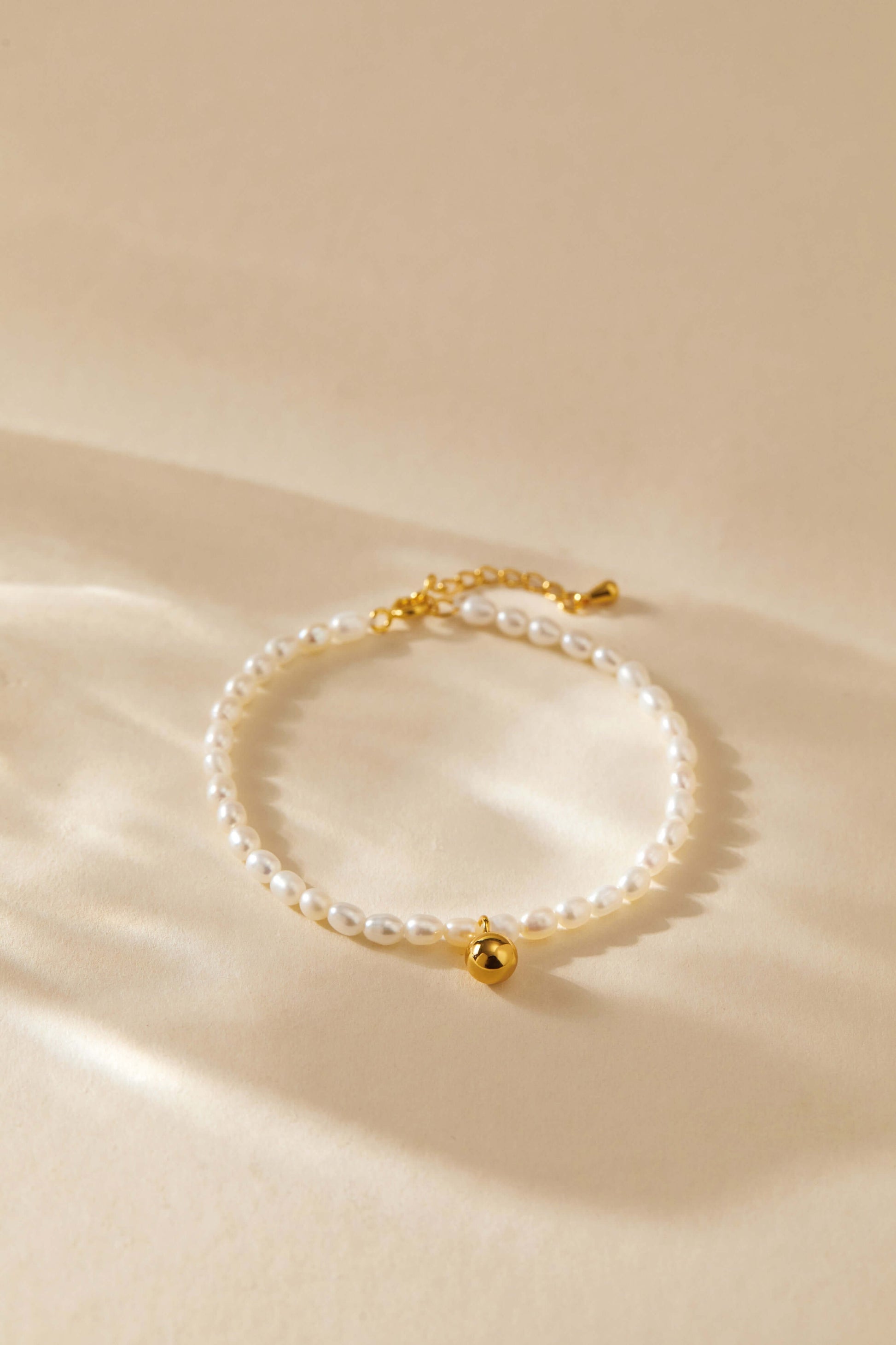 Celestia Freshwater Pearl Bracelet by SUIHE Jewelry with gold-tone bead charm on beige background.
