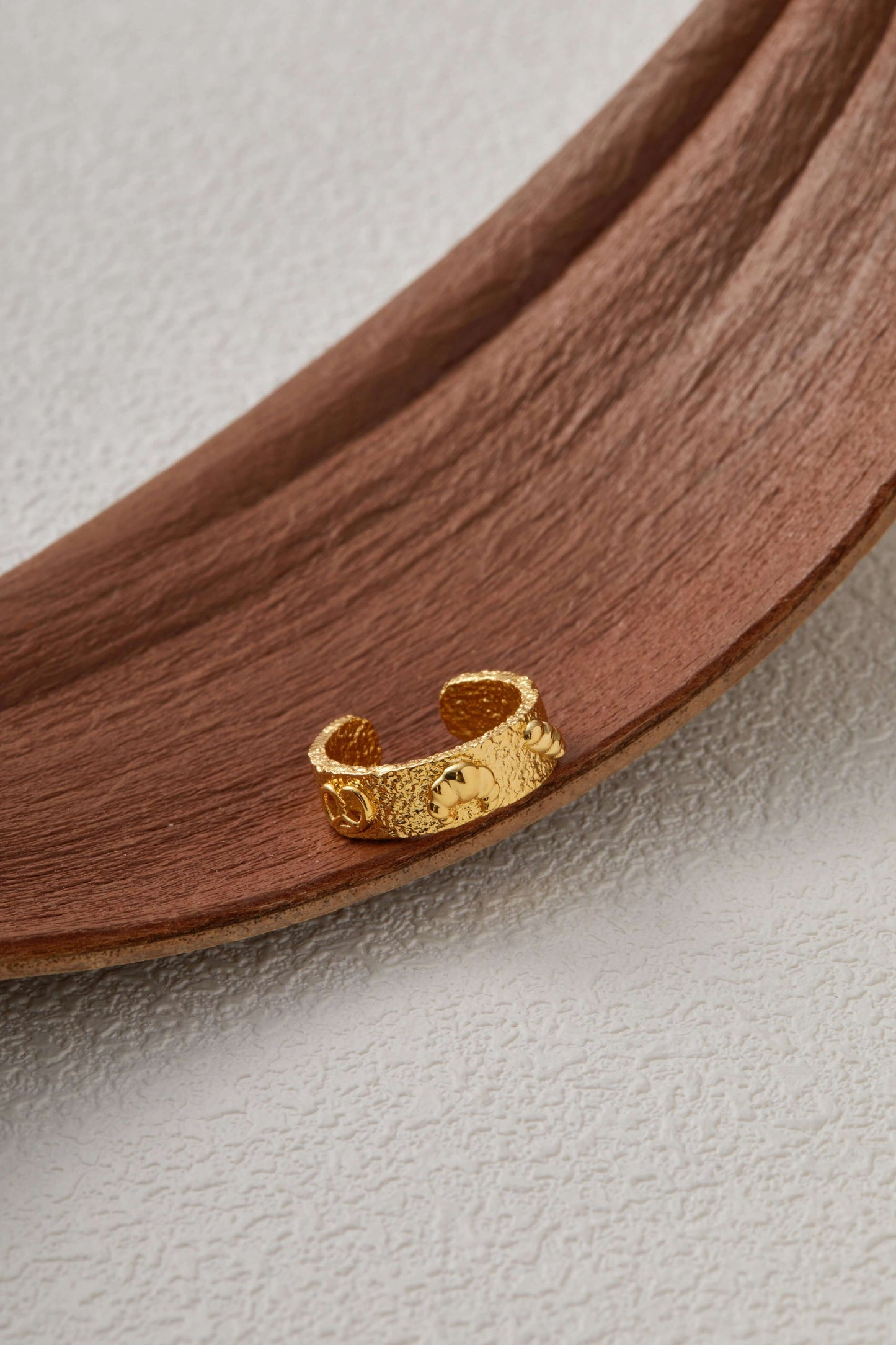 18k gold vermeil ring with croissant, pretzel and baguette charms, inspired by bread platter, on a rustic wooden surface.