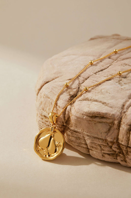 Gold pear-shaped pendant necklace by SUIHE Jewelry with bead accents on a textured stone background, highlighting its refined elegance.