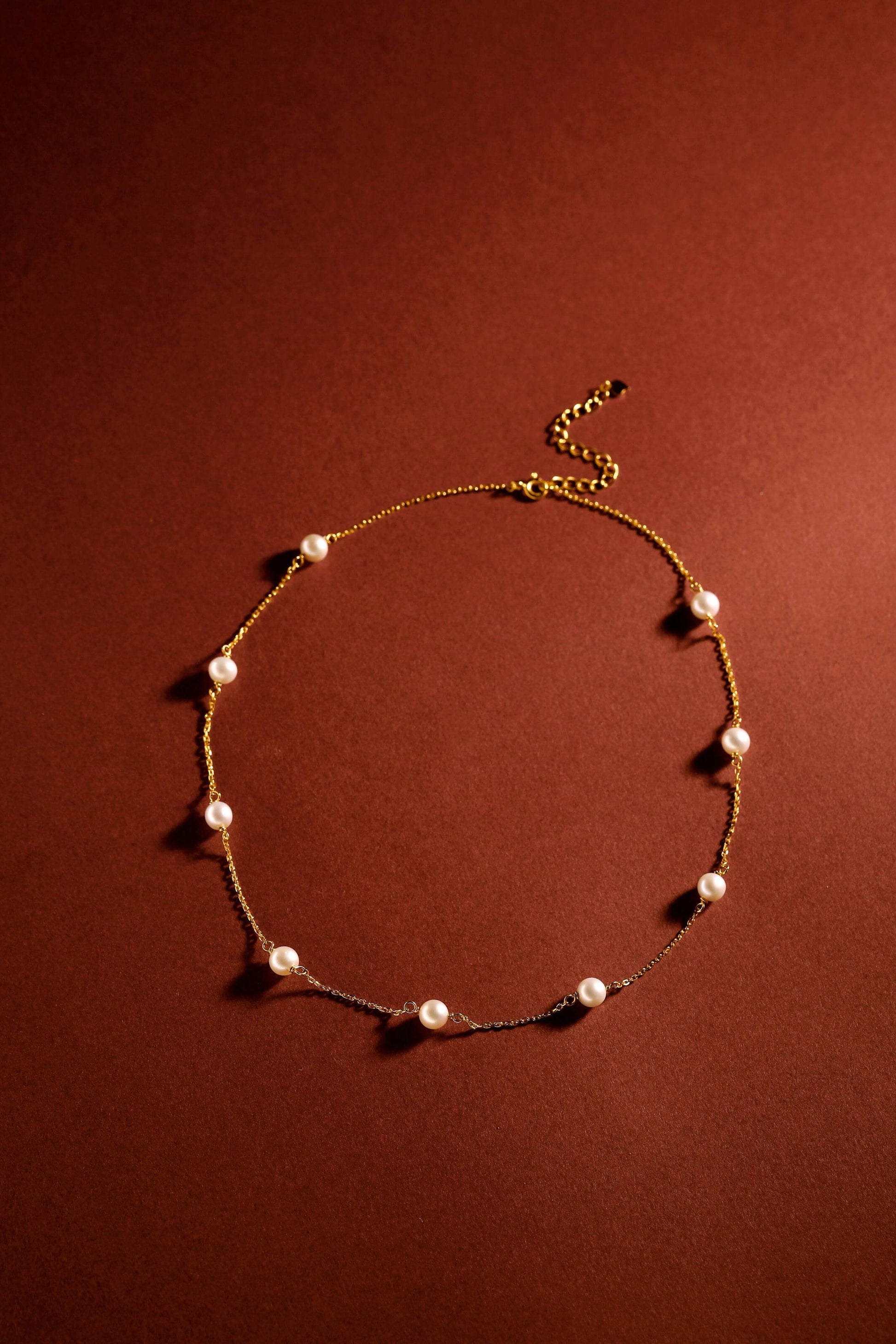 Starry Night Akoya Pearl Necklace by SUIHE Jewelry, featuring lustrous pearls on a delicate chain against a warm brown background.