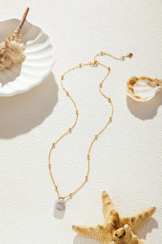 Gold-plated aquamarine stone necklace with zircon, SUIHE Jewelry on sand with seashells.