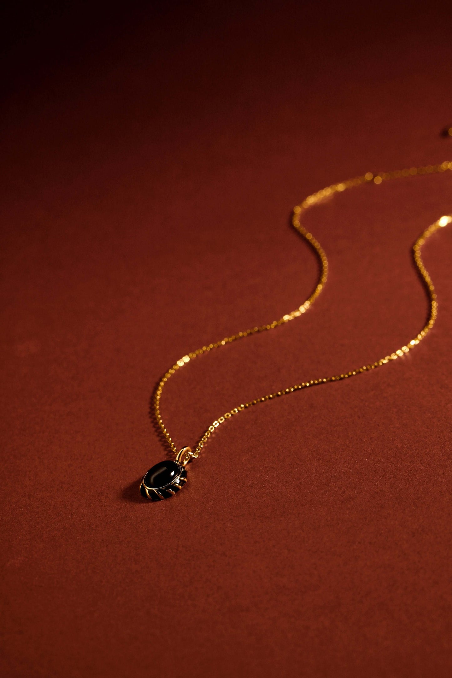 "Eclipse Necklace by SUIHE Jewelry with black onyx pendant and gold vermeil chain against a warm brown background"