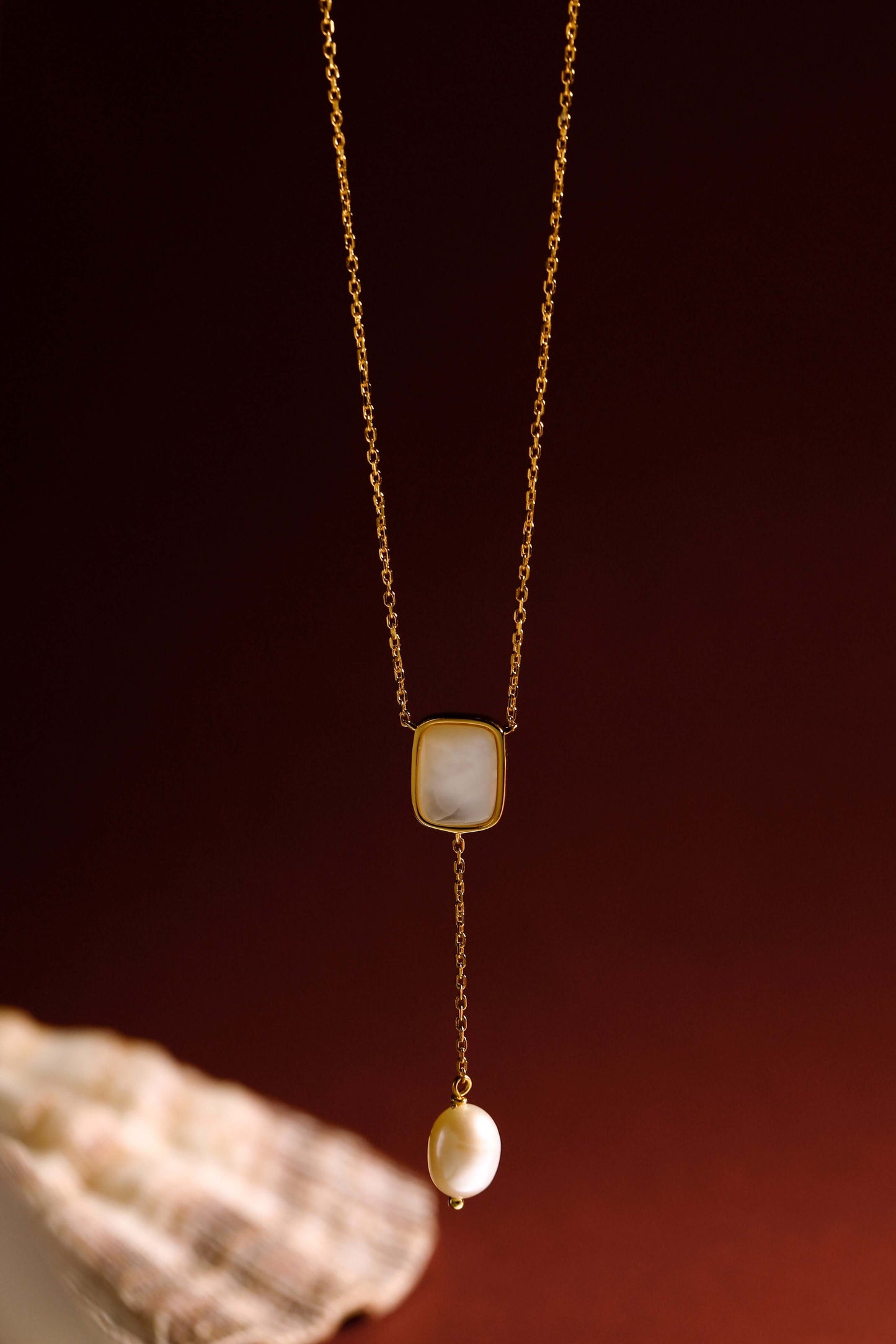 Gold chain necklace with a mother-of-pearl pendant and pearl drop, featuring SUIHE Jewelry's "Allure" design against a dark background.