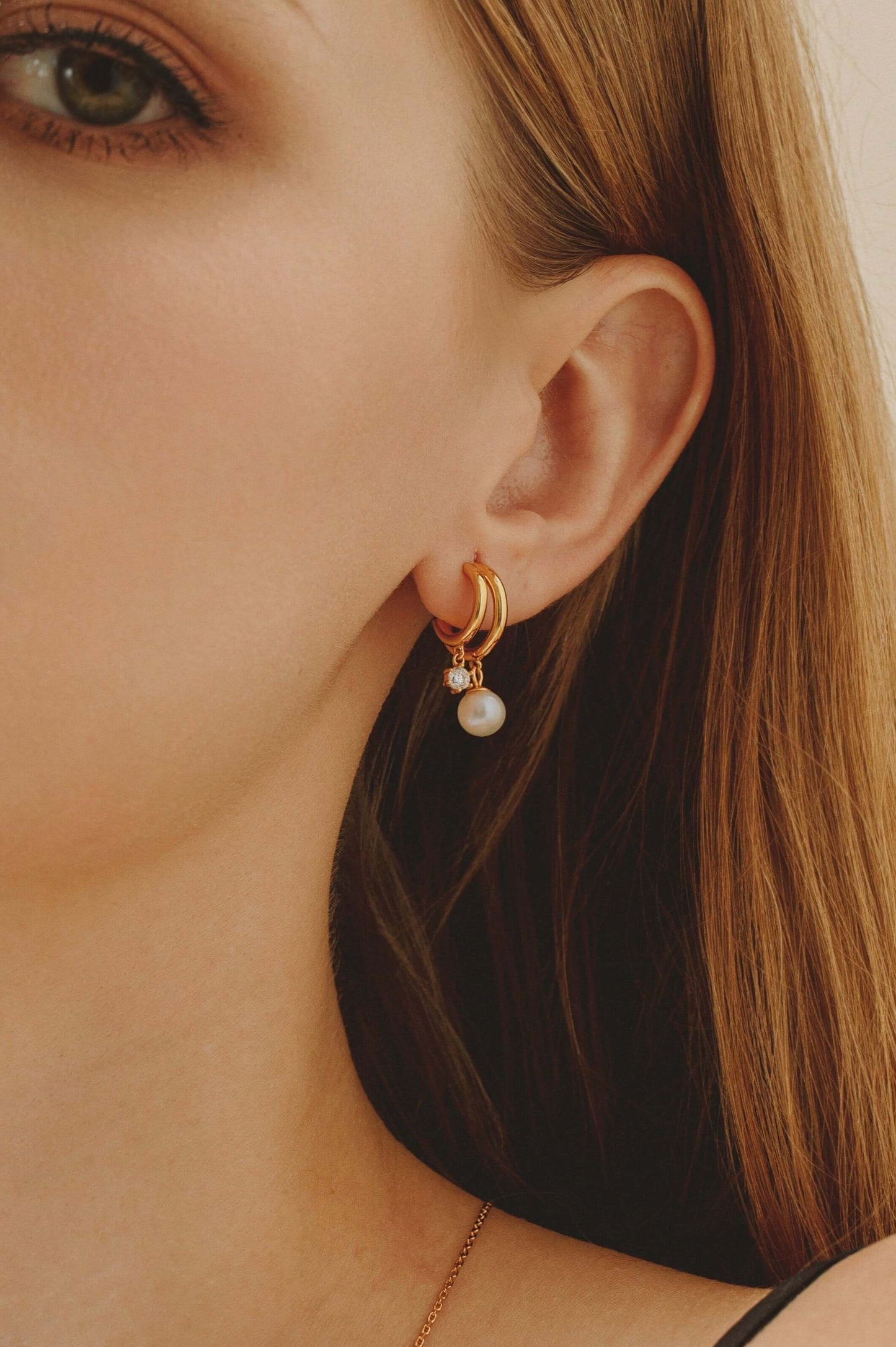Close-up of woman wearing SUIHE Jewelry 'Allure' freshwater pearl earrings with zircon stones and 18k gold vermeil double semi-circle design.