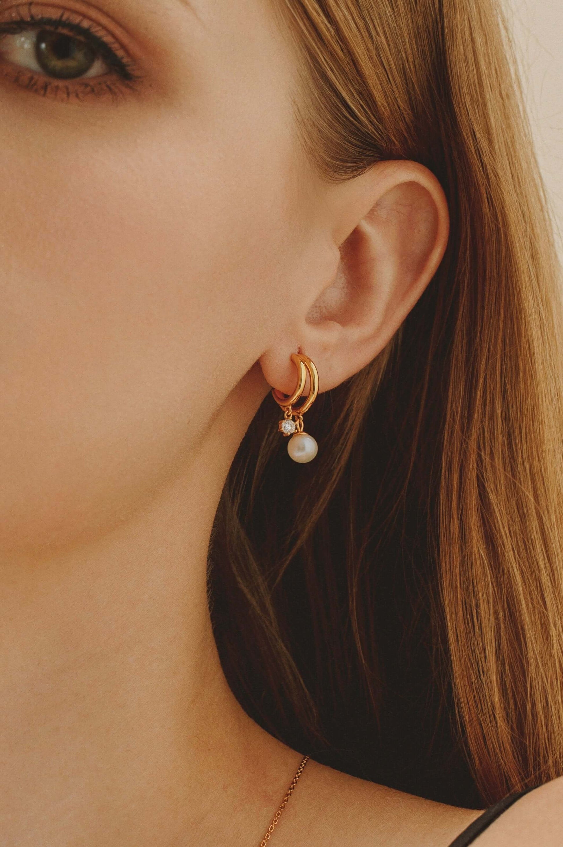 Close-up of woman wearing SUIHE Jewelry 'Allure' freshwater pearl earrings with zircon stones and 18k gold vermeil double semi-circle design.