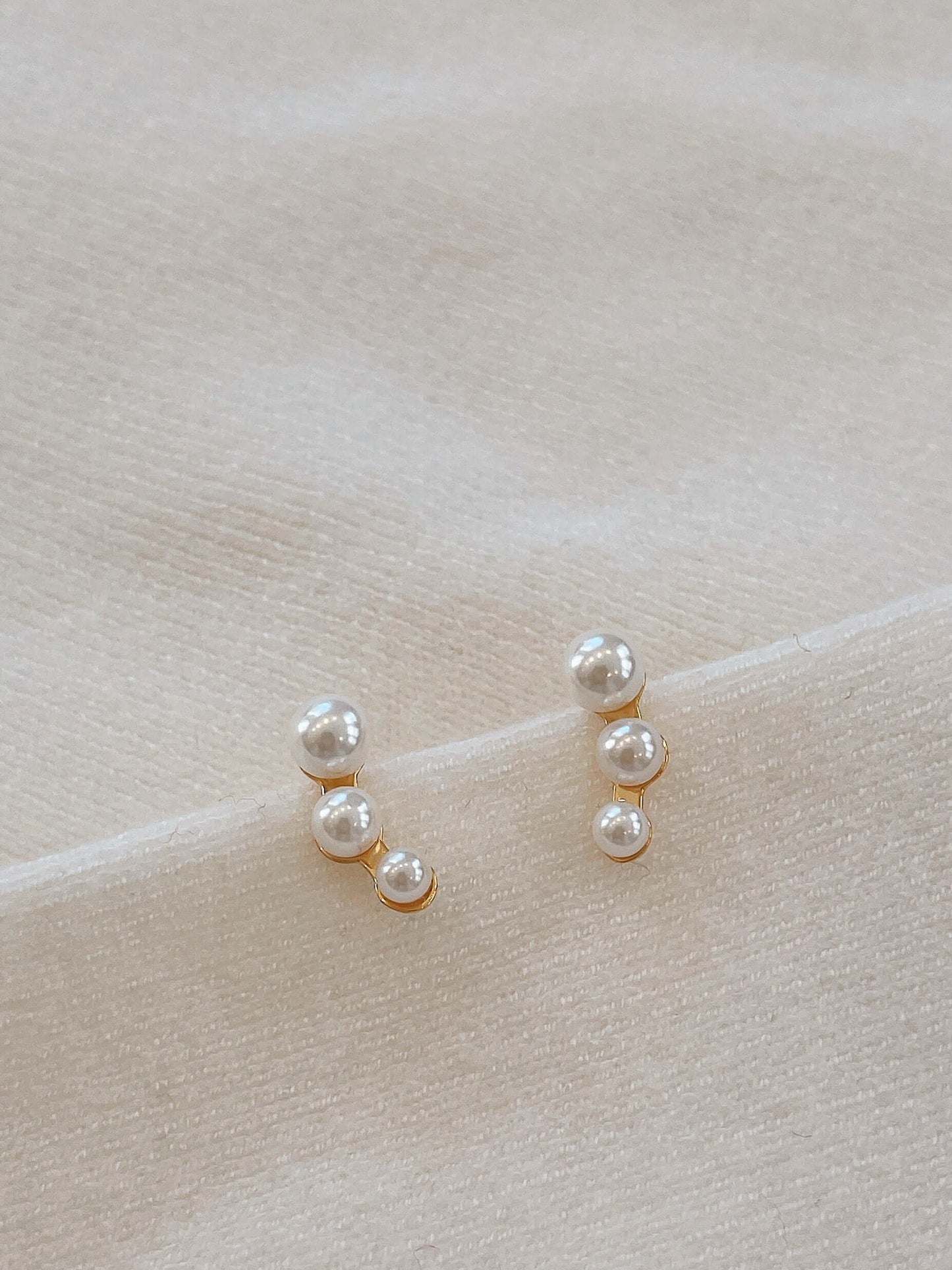 "Flare" freshwater pearl earrings by SUIHE Jewelry with 18k gold vermeil on soft fabric background.