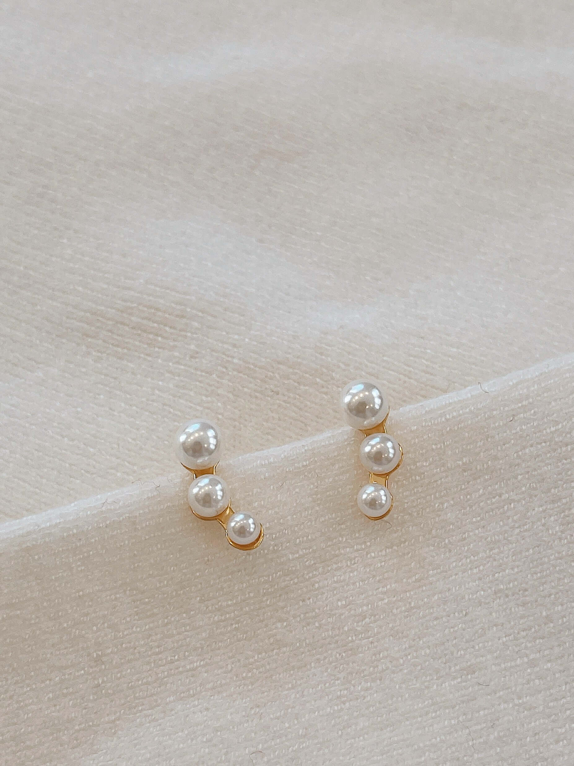 "Flare" freshwater pearl earrings by SUIHE Jewelry with 18k gold vermeil on soft fabric background.