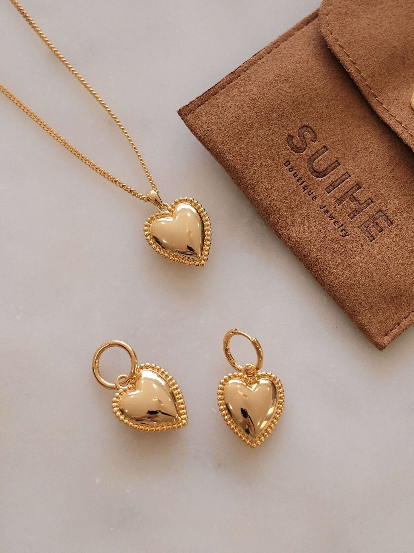 SUIHE Jewelry gold-tone heart charm hoop earrings and necklace set with beaded detailing on a marble surface.