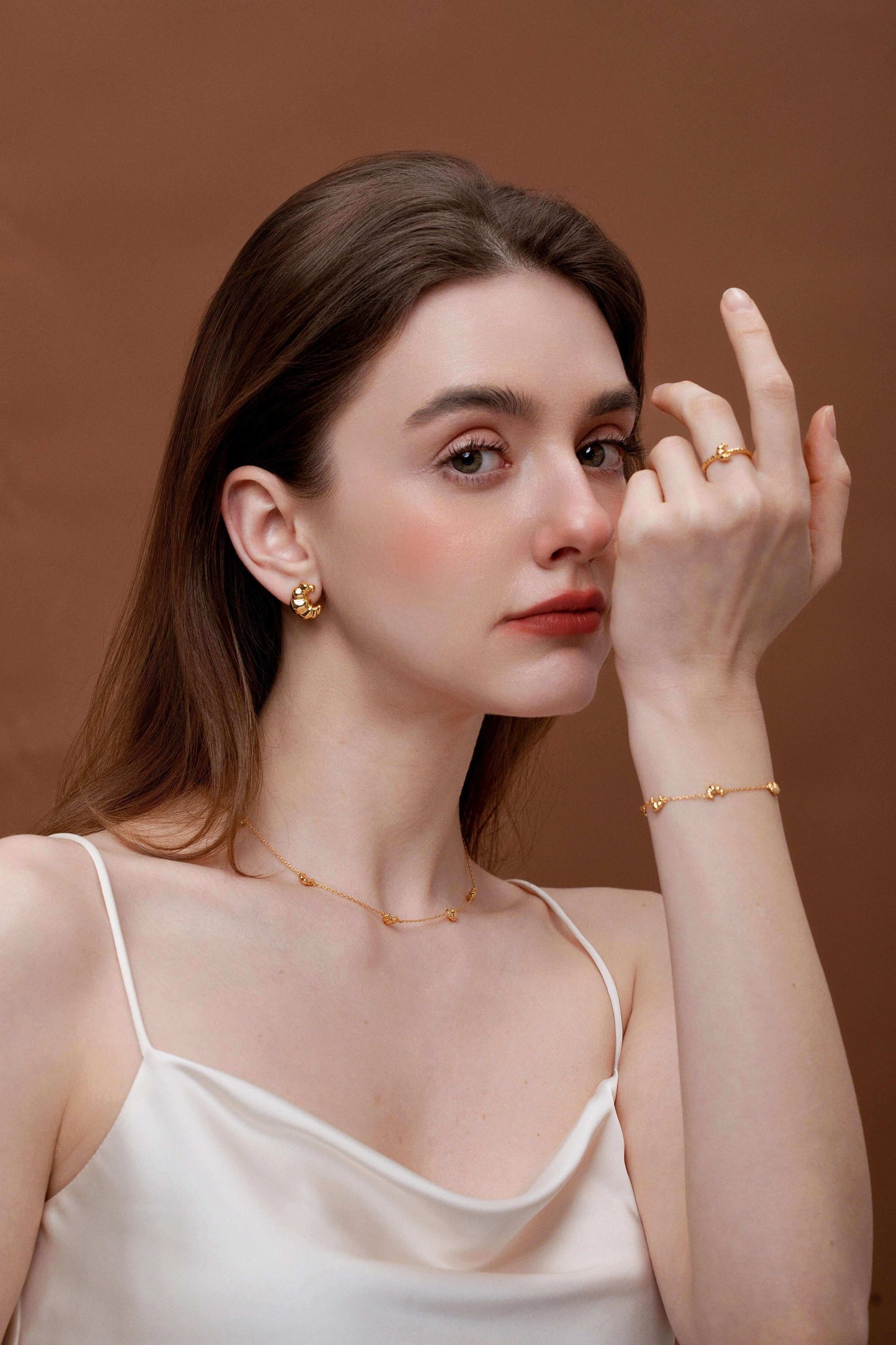 Woman wearing SUIHE Jewelry with elegant gold open cuff croissant ring, matching earrings, necklace, and bracelet on a brown background.