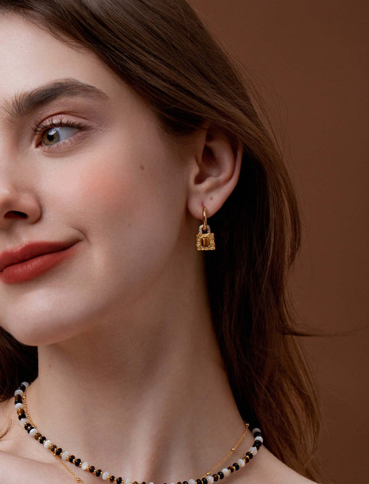 Woman wearing SUIHE Jewelry gold-plated huggie hoops with lock pendants and Tiger Eye stone, symbolizing strength and elegance.