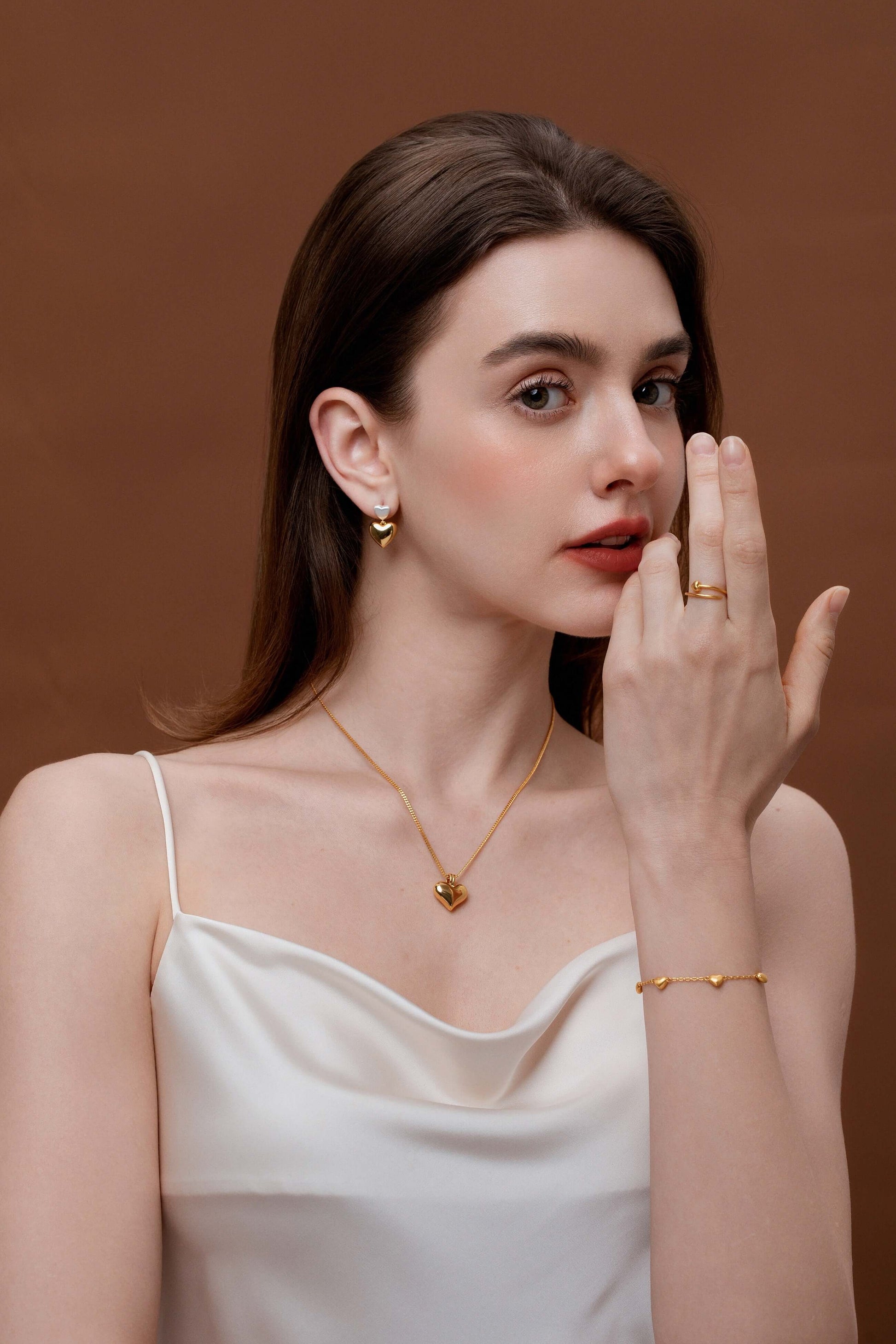 Woman wearing stylish jewelry, including a necklace, bracelet, and earrings on a brown background, showcasing an elegant fashion look.