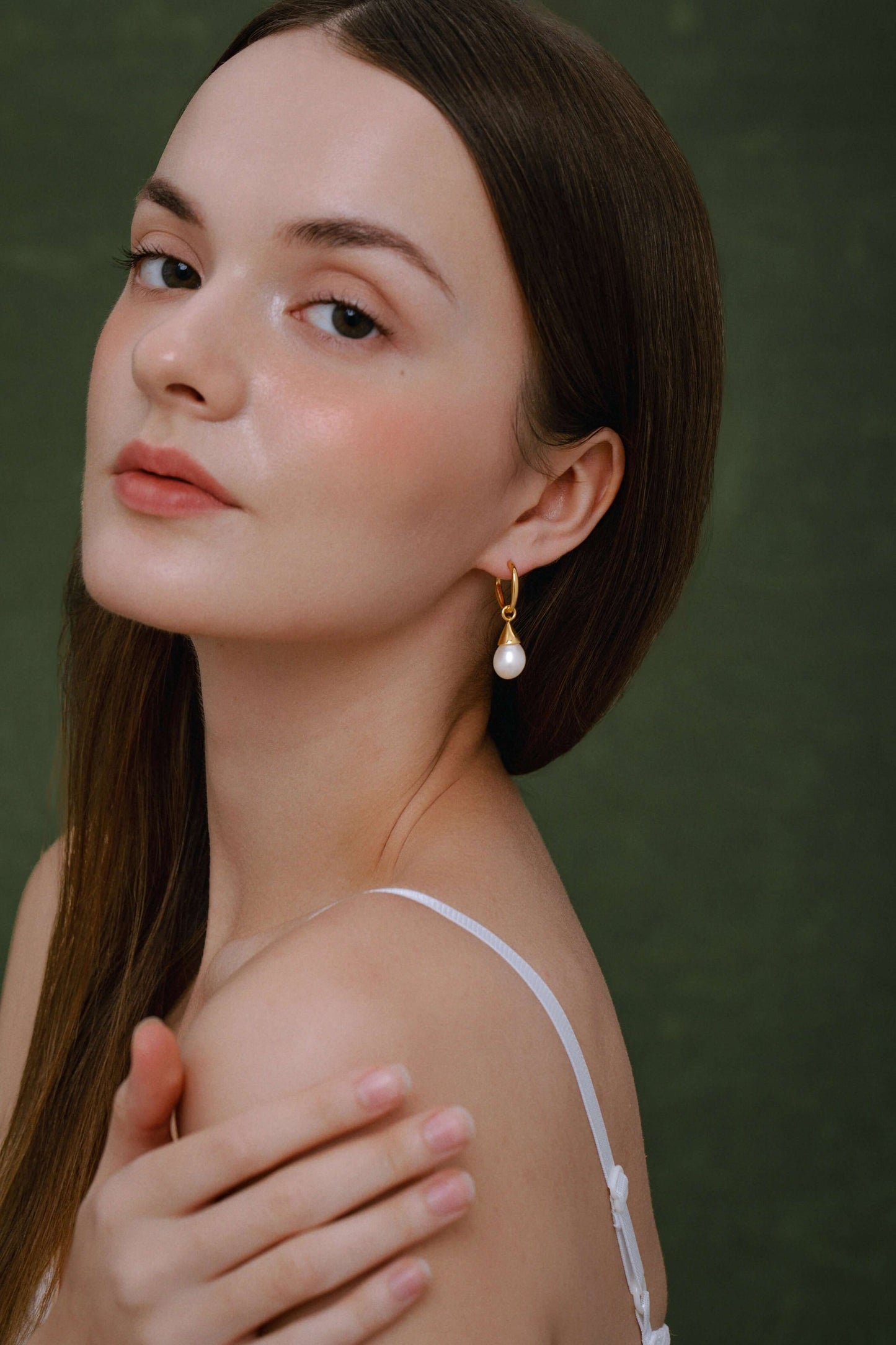 Woman wearing Dewdrop Freshwater Pearl Earrings in gold from SUIHE Jewelry, showcasing elegance against a dark green background.