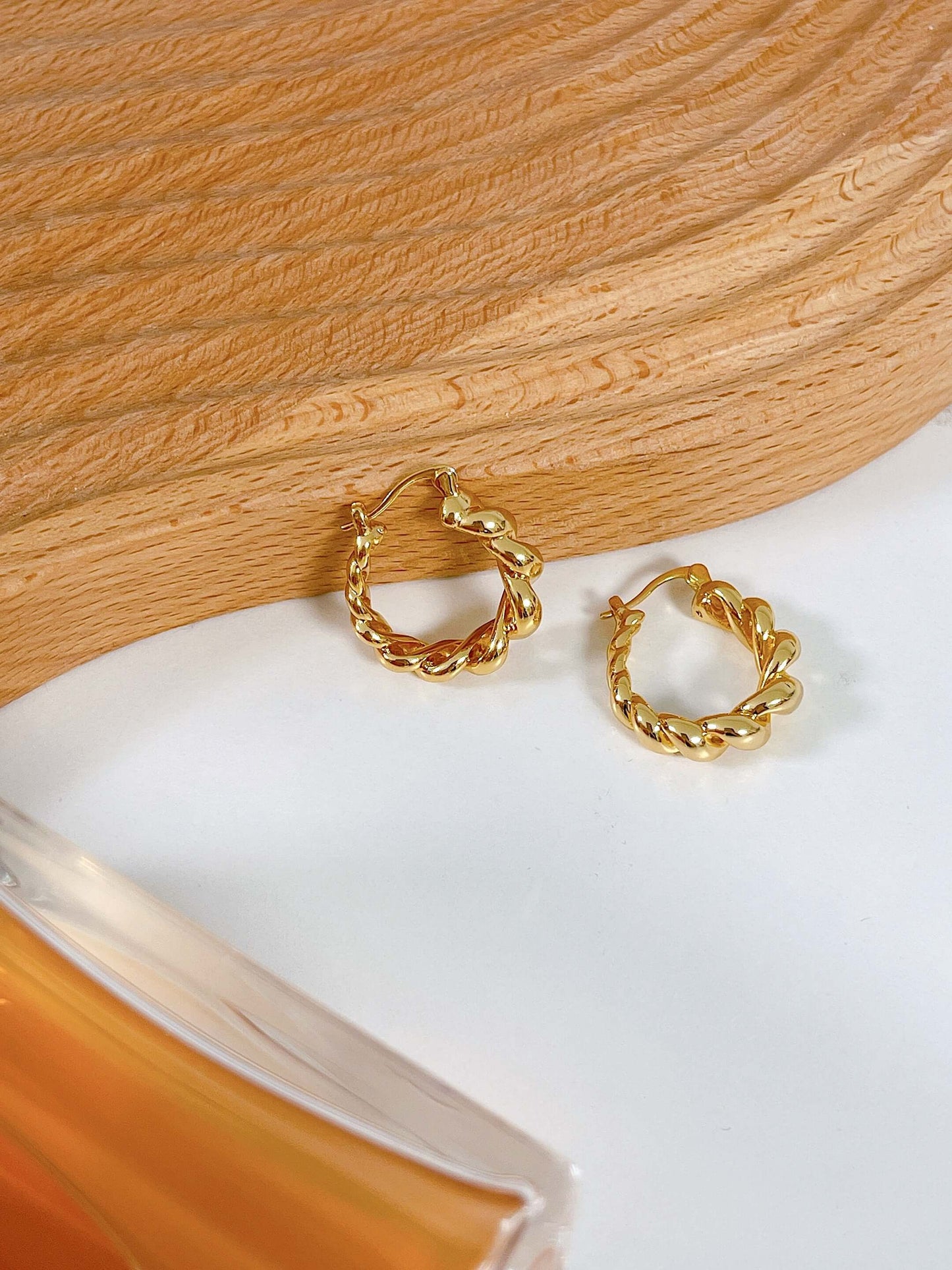 SUIHE Jewelry "Everyday Simplicity" twisted hoop earrings in 18k gold-filled copper on a wooden background.