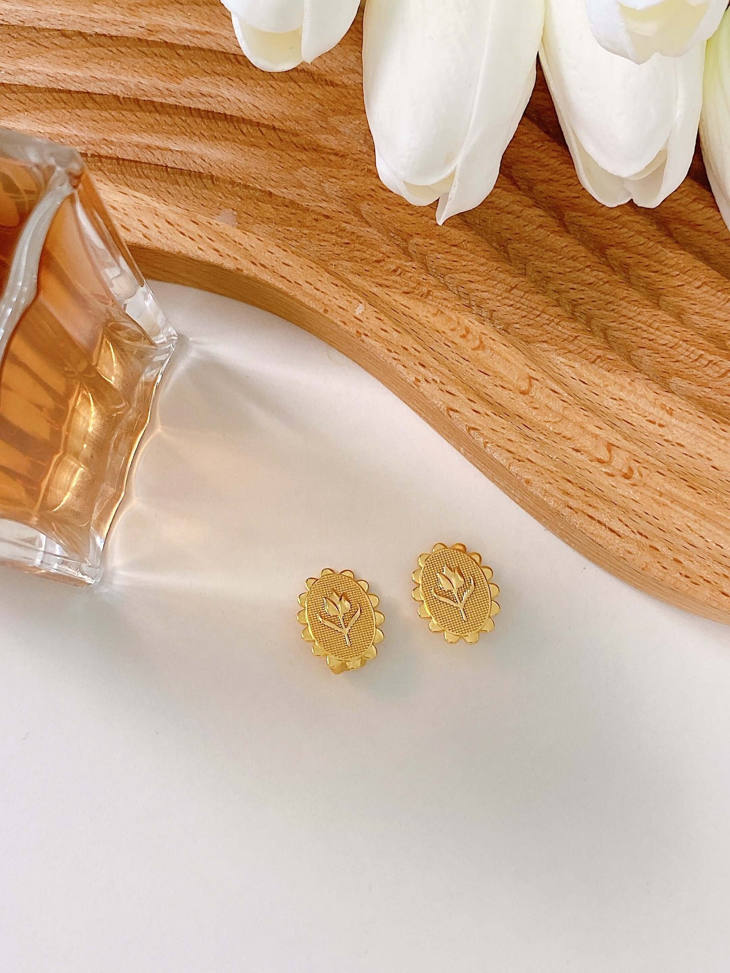 Golden Tulip clip earrings by SUIHE Jewelry in 18k gold vermeil, showcasing tulip embossed design, placed on a wooden surface with white flowers.