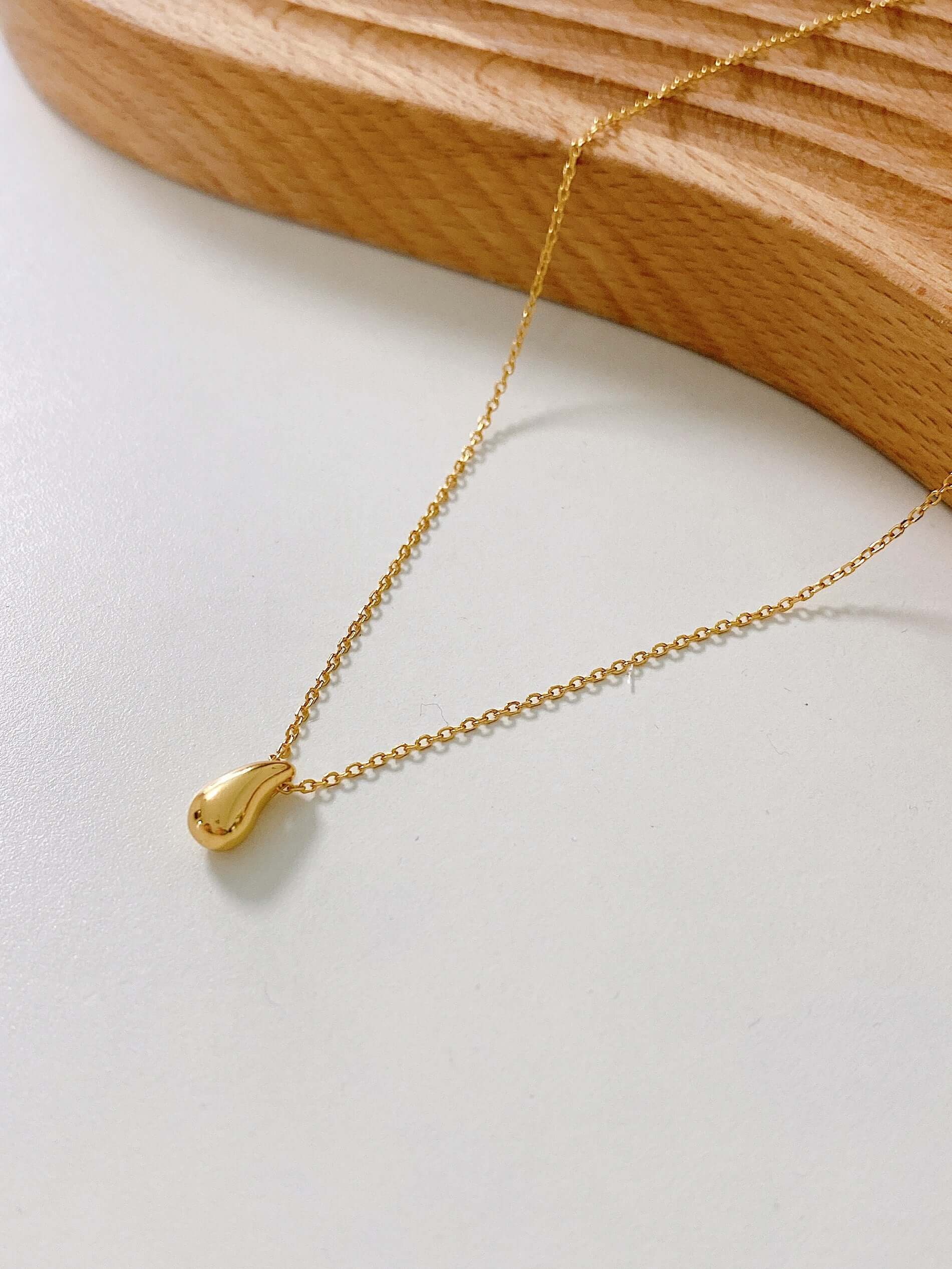 18k Gold Vermeil "Teardrop" Necklace by SUIHE Jewelry resting on a wooden surface, symbolizing resilience and elegance.