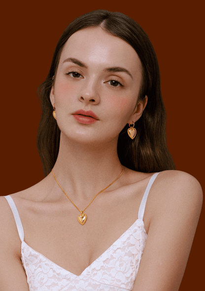 Woman wearing SUIHE Jewelry gold-tone heart charm hoop earrings and pendant necklace, showcasing elegance and romance.