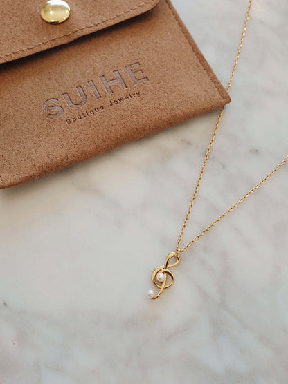 Aria necklace with music note charm in 18k gold vermeil by SUIHE Jewelry, displayed on a marble surface with pouch.