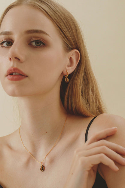 Woman wearing 'Mocha' Pendant Earrings by SUIHE Jewelry, showcasing 18k gold-plated silver with yellow enamel and tiger's eye stone.
