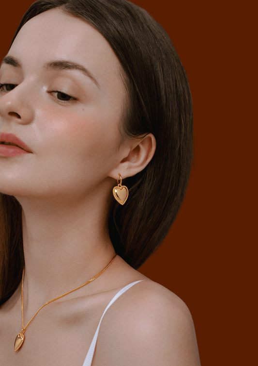 Woman wearing Adore Heart Charm Hoop Earrings by SUIHE Jewelry, featuring gold-tone heart pendants with beaded detailing.
