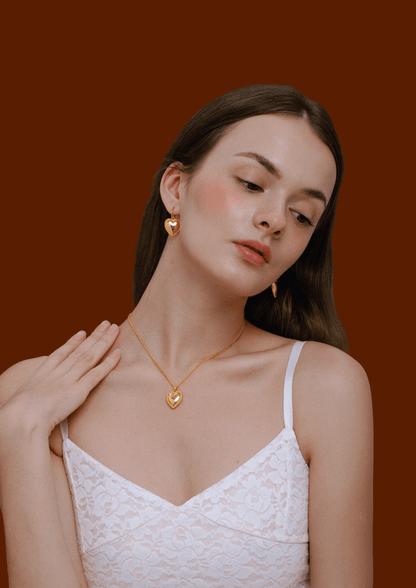 Golden heart charm hoop earrings by SUIHE Jewelry worn by a model in white lace top, showcasing elegance and romantic style.