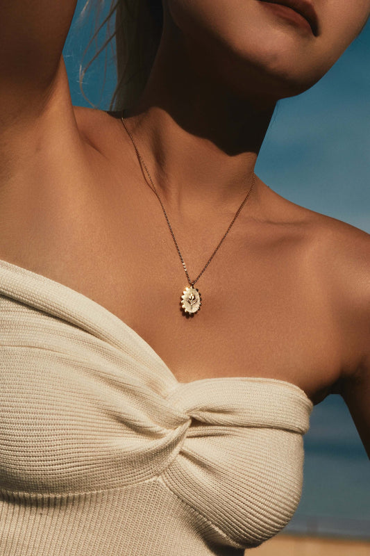 Woman wearing golden tulip necklace, SUIHE Jewelry, in elegant off-shoulder top against a blue sky background.