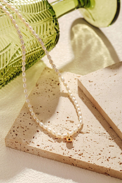 Celestia Freshwater Pearl Necklace by SUIHE Jewelry with 3-4mm pearls and 18k gold vermeil, displayed on textured tiles.