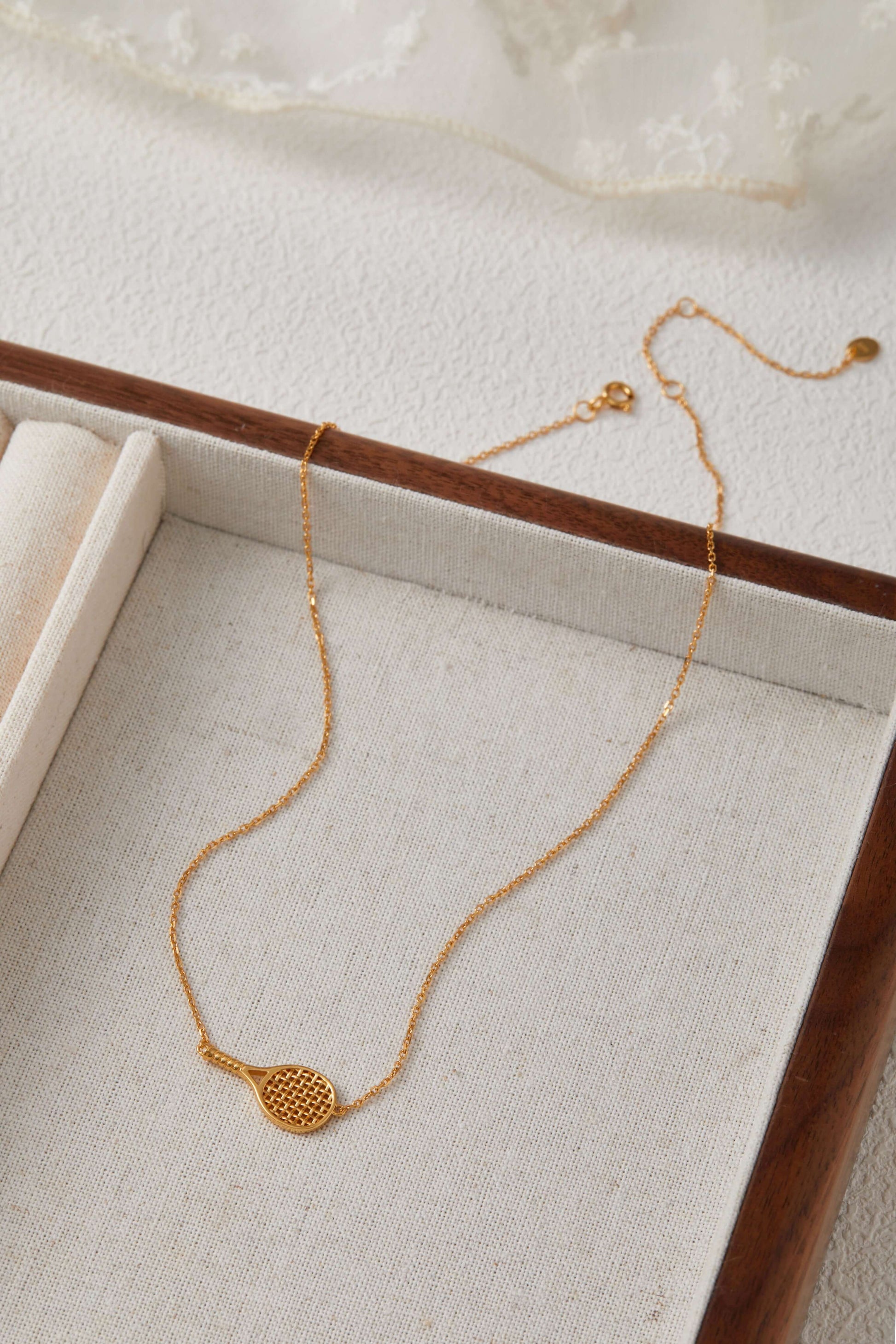 Gold-plated tennis racket necklace by SUIHE Jewelry on a display box, combining sporty chic with elegant style.