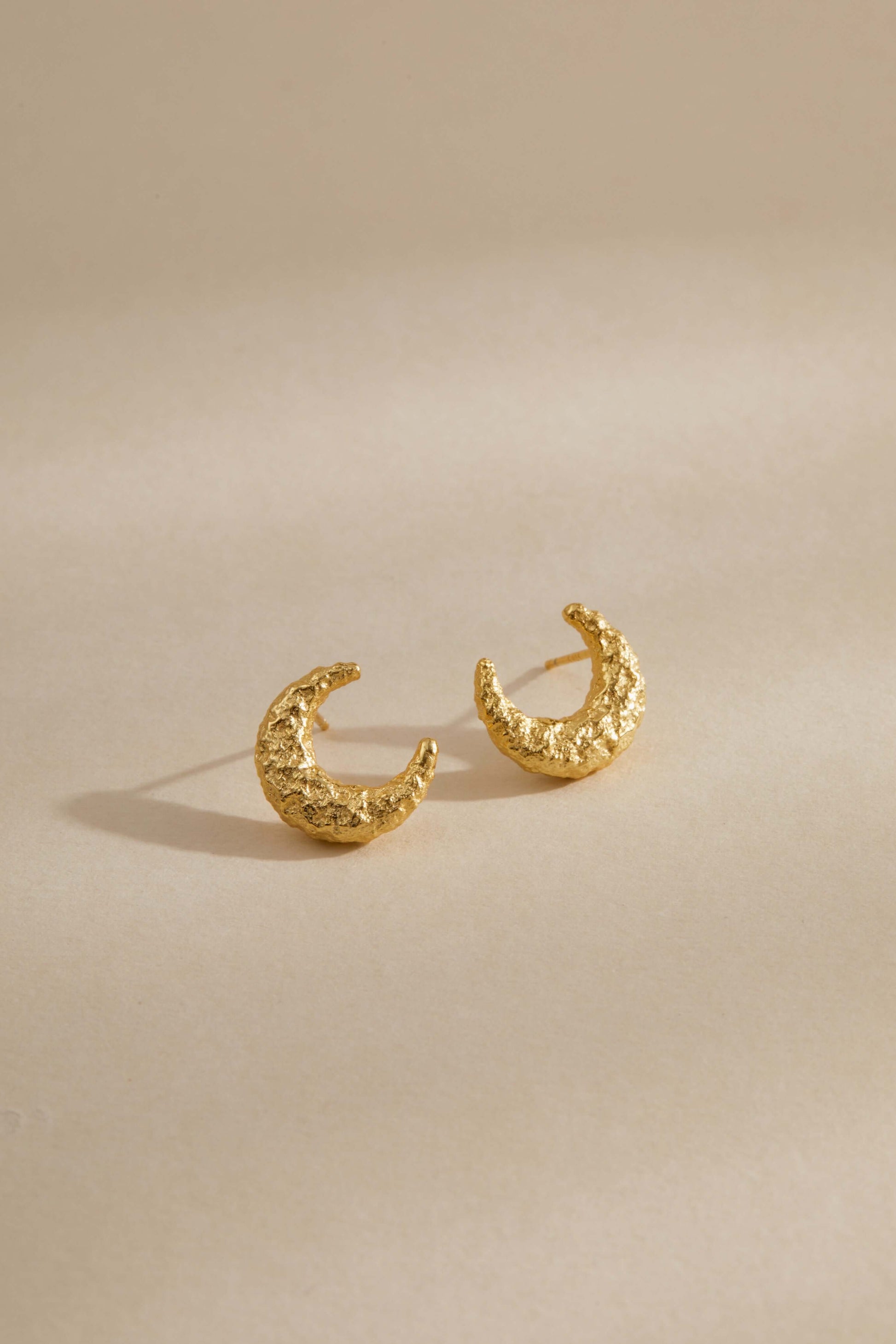 Gold-plated textured crescent moon earrings by SUIHE Jewelry on a beige background.