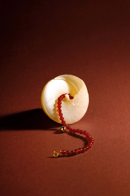 SUIHE Jewelry 'Lucky' Red Agate Gemstone Bracelet with 18k Gold Vermeil displayed with seashell on a warm brown background.