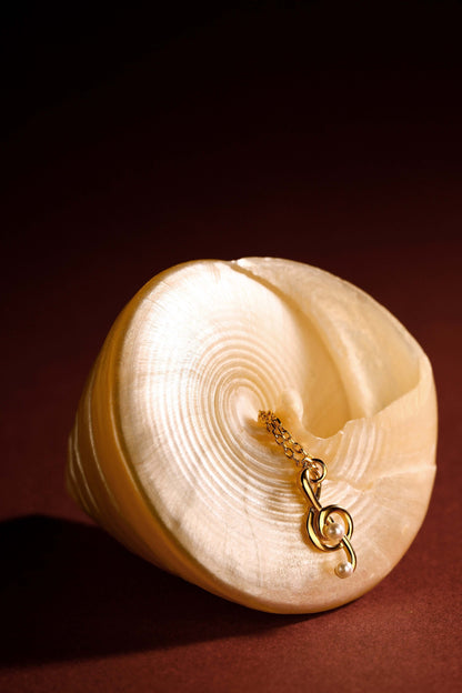 Aria Necklace by SUIHE Jewelry, featuring an 18k gold vermeil music note charm on a smooth, light shell background.