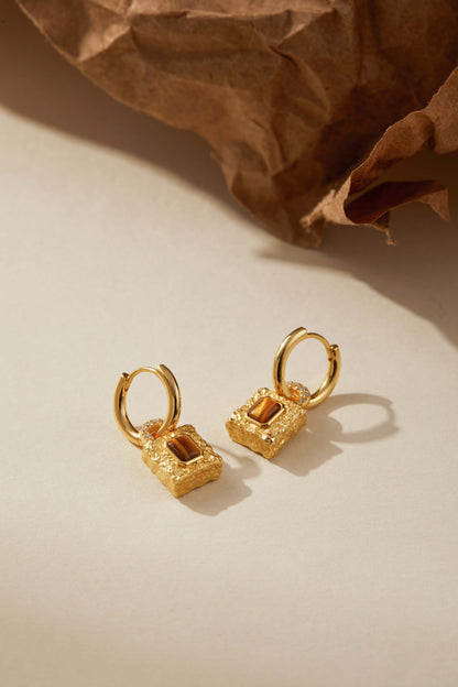 SUIHE Jewelry Lock Tiger Eye Stone Earrings, gold-plated huggie hoops with textured lock pendants and Tiger Eye stones, on paper backdrop.