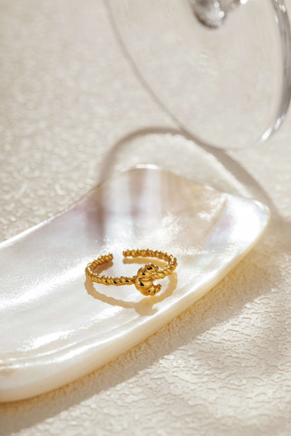Gold-plated open cuff ring by SUIHE Jewelry with a croissant-inspired twisted design on a textured surface.