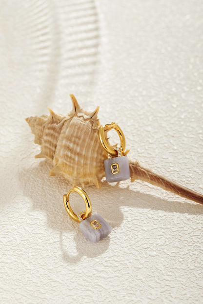 SUIHE Jewelry gold-plated hoops with aquamarine lock pendants, accented by zircon. Earrings displayed on a textured shell.