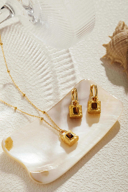 Gold-plated lock pendant necklace and earrings with Tiger Eye stones on a tray, SUIHE Jewelry, promoting confidence and resilience.