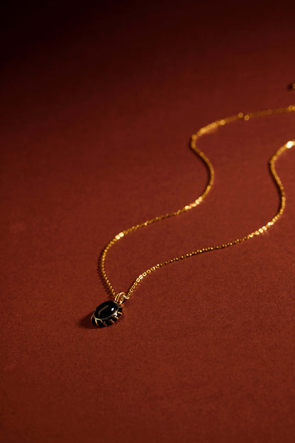 "Eclipse Necklace by SUIHE Jewelry with black onyx pendant and gold vermeil chain against a warm brown background"