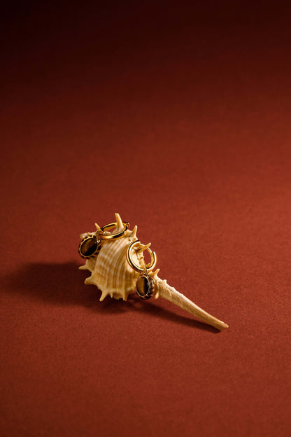 Mocha Pendant Earrings by SUIHE Jewelry displayed on a seashell, featuring 18k gold-plated silver, yellow enamel, and tiger's eye stones.