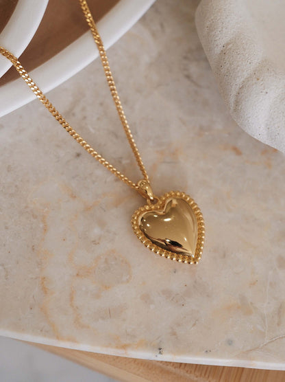 Gold heart charm necklace with beaded detailing on a stone surface; Adore Necklace by SUIHE Jewelry symbolizing love and elegance.