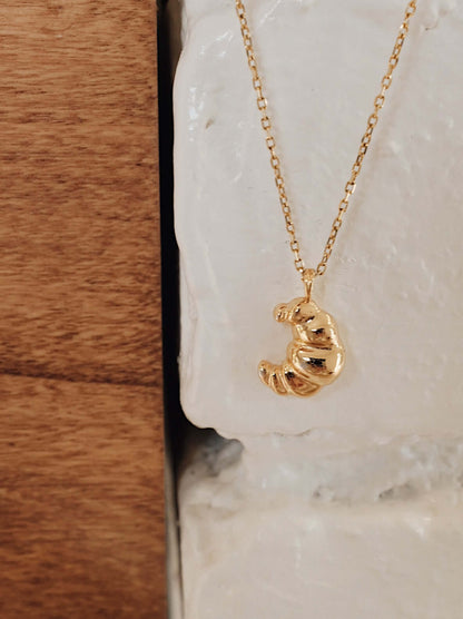 Gold vermeil croissant-shaped necklace by SUIHE Jewelry, evoking Parisian elegance with its textured design, hanging against a stone wall.