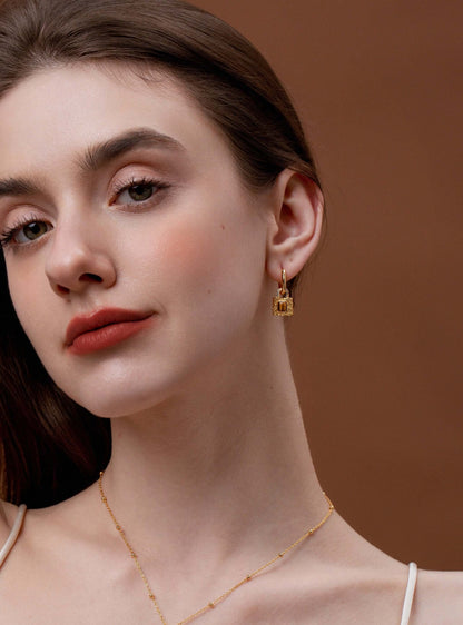 Close-up of woman wearing SUIHE Jewelry's Lock Tiger Eye Stone Earrings, featuring gold-plated hoops and a textured lock pendant with Tiger Eye stone.