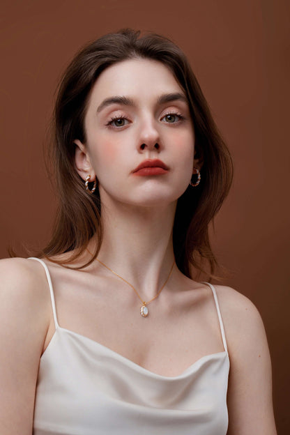 Young woman wearing SUIHE Jewelry Dough Twist Hoop Earrings in gold and white enamel, styled with a white top, against a brown background.